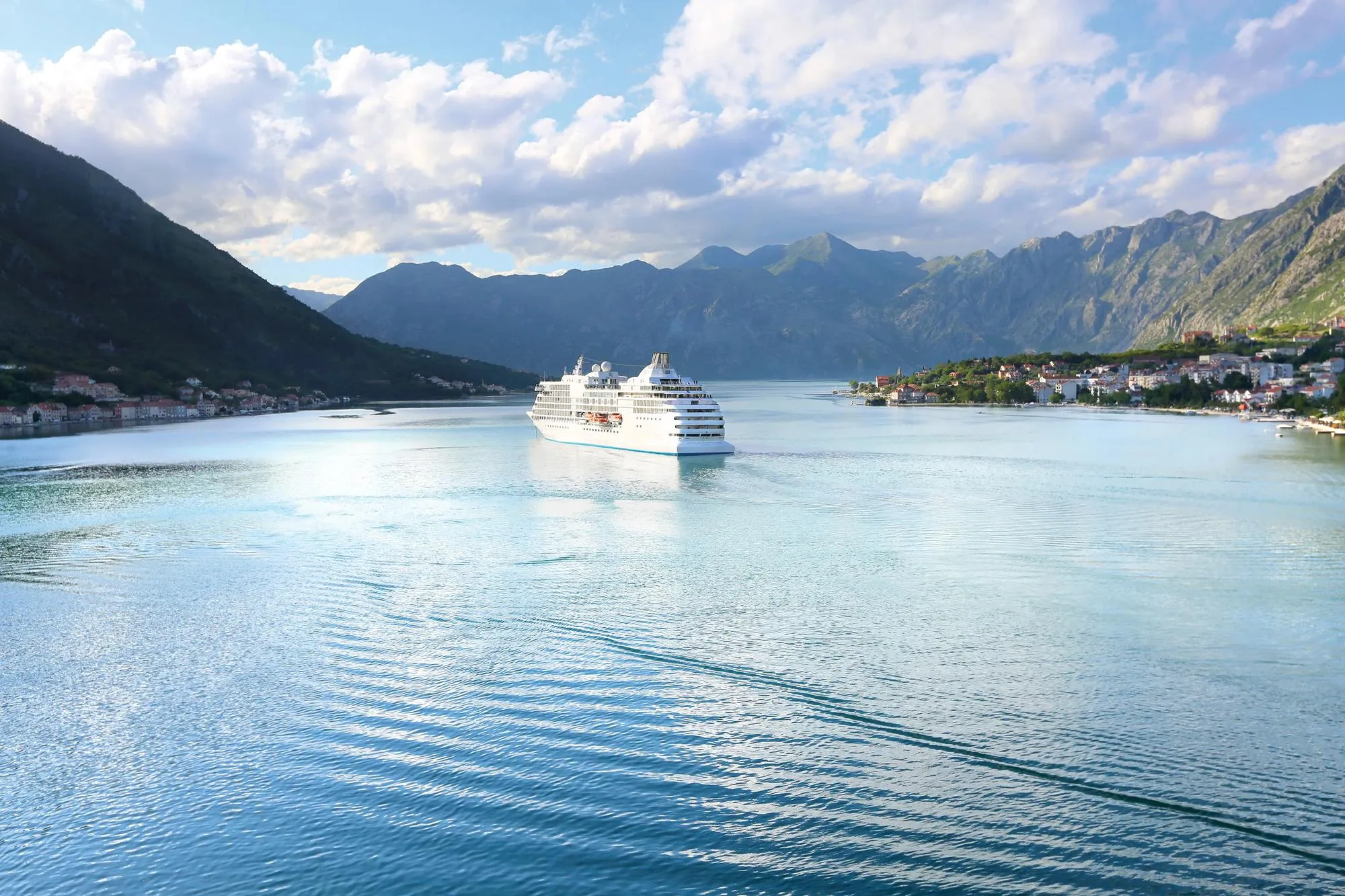 A white expedition ship sailing a mountain-ringed bay on calm turquoise water