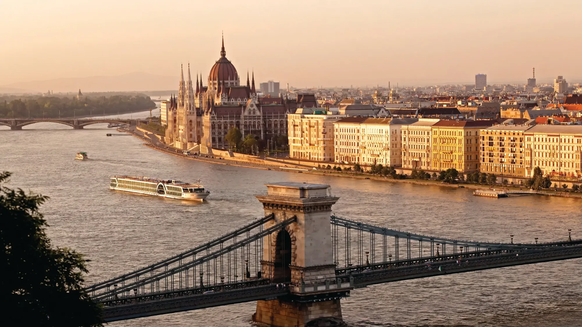 A river ship on the Danube in Budapest with the Parliament building and a chain bridge at sunset