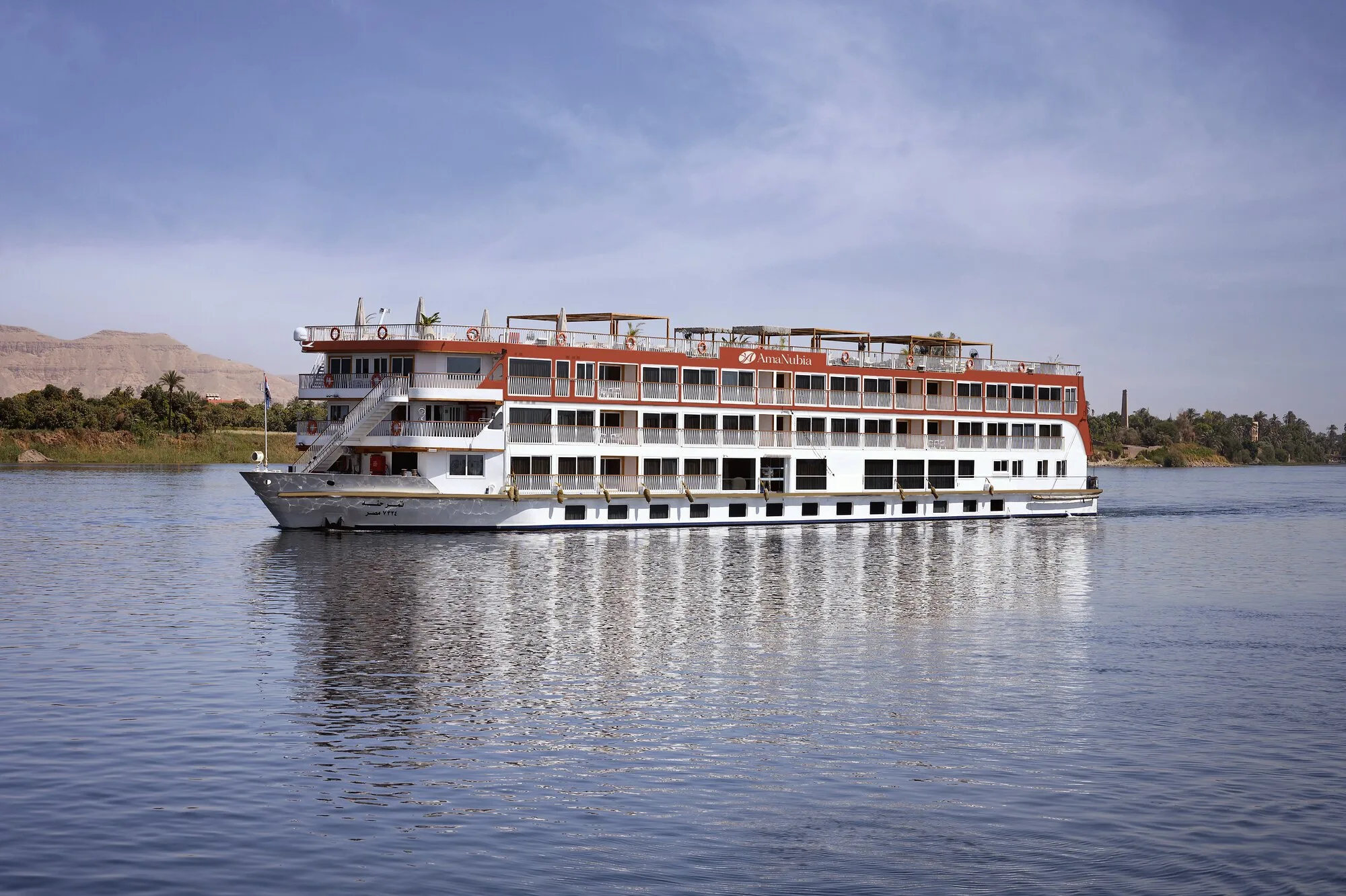 A white river ship cruising a wide calm river beneath a pale sky