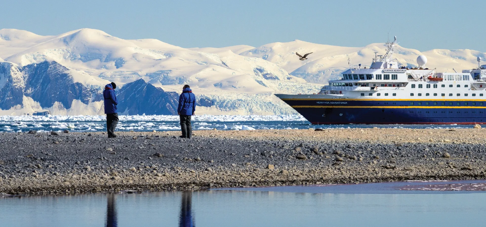 Expedition ship beyond a shoreline with snow-covered mountains